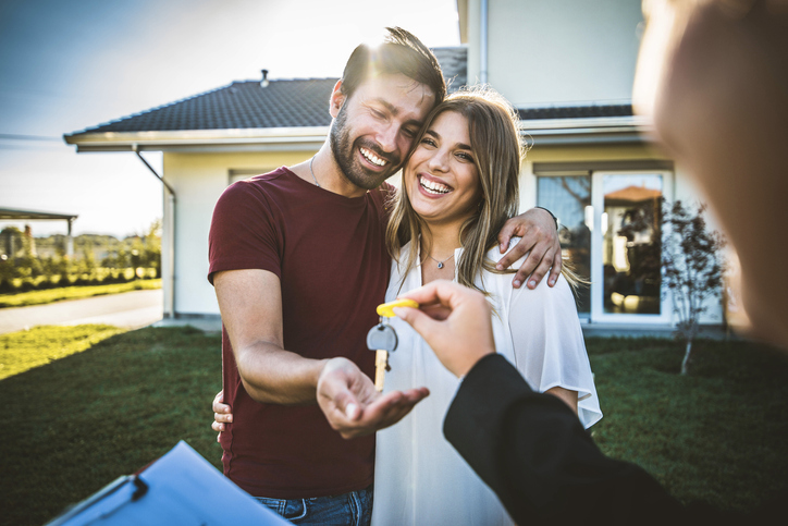 Happy millennial couple receiving keys from Real Estate Agent, purchasing real estate